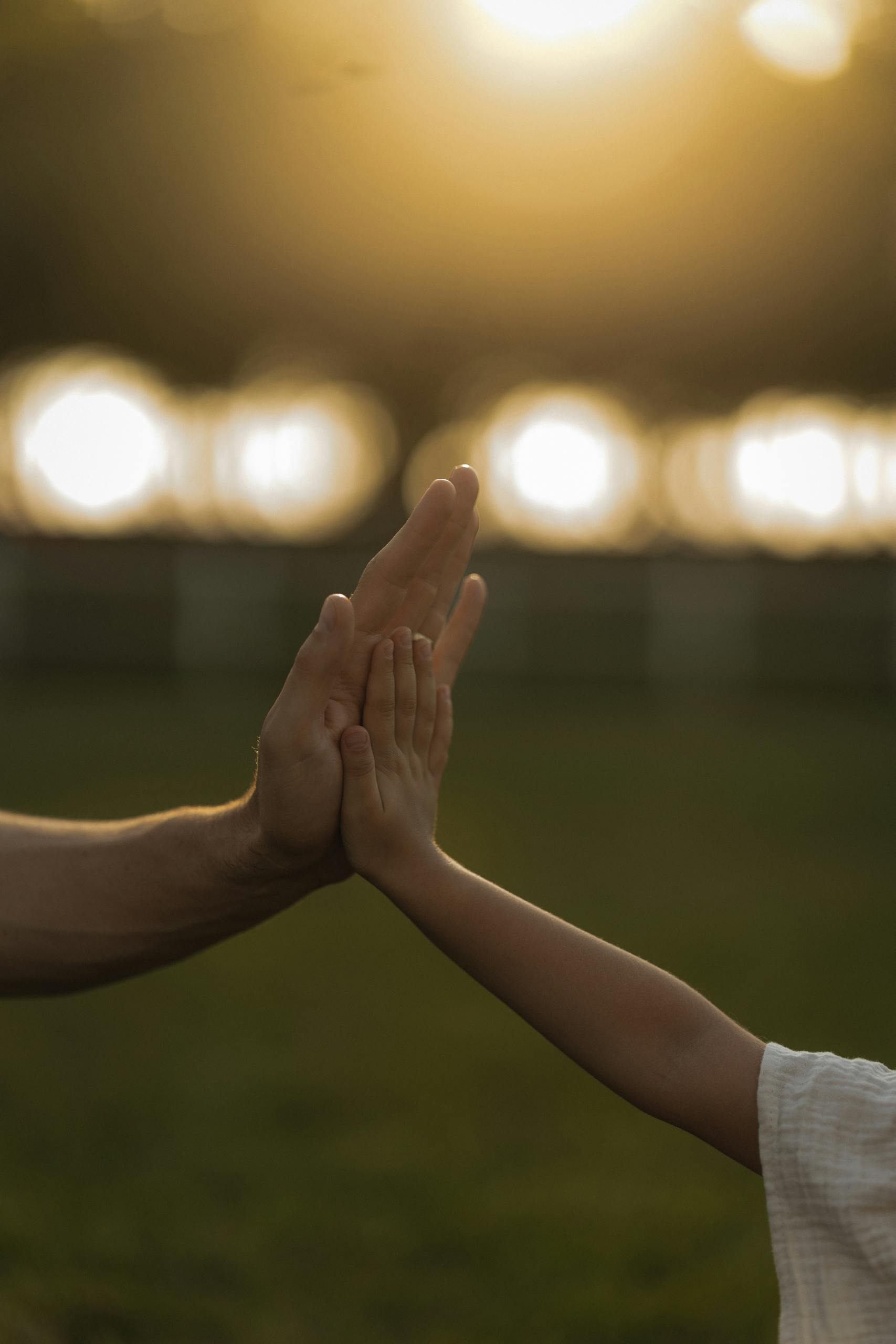 A touching moment of a father and child sharing a high five outdoors during sunset.