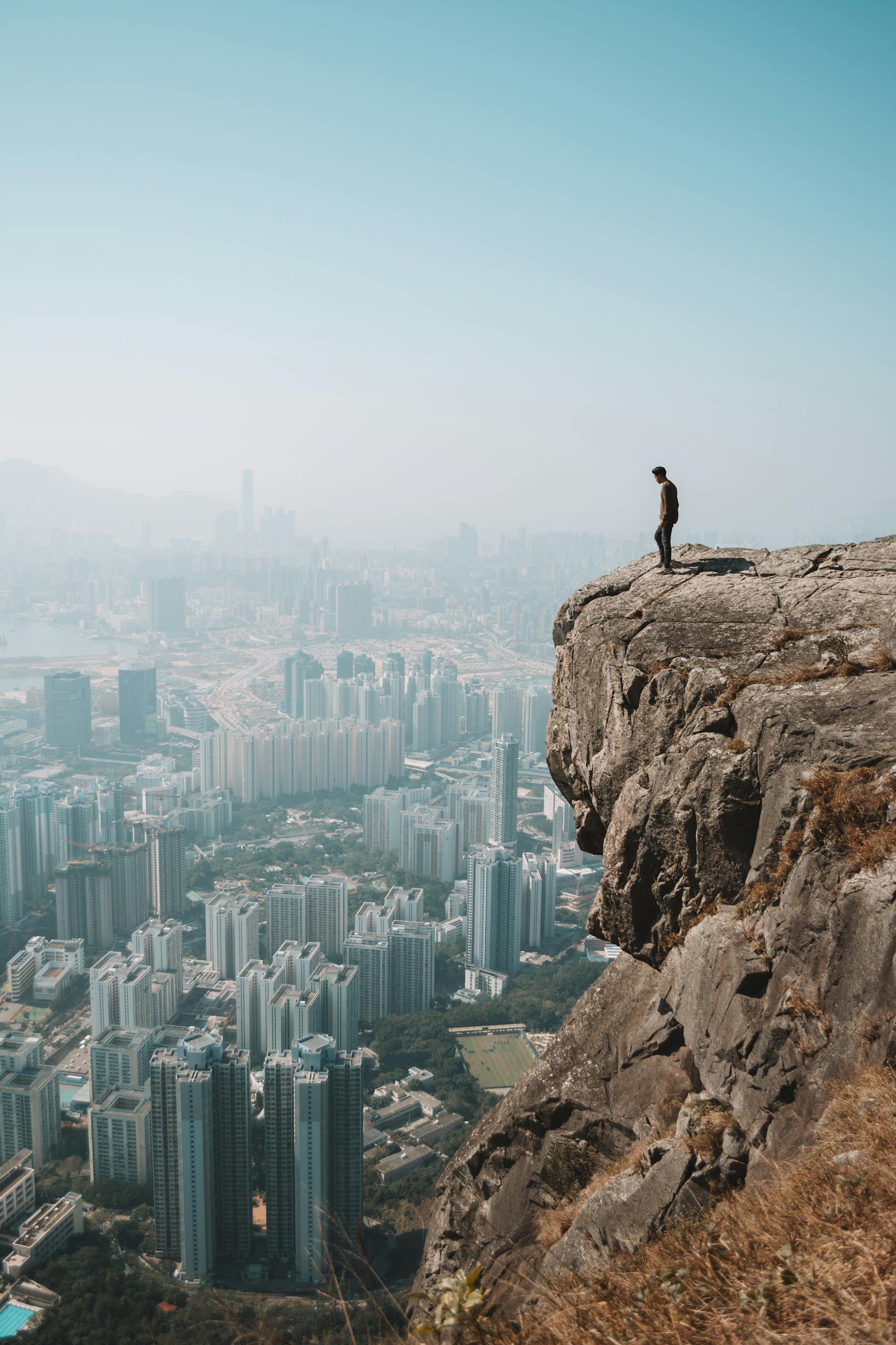 Man stands on cliff overlooking stunning Hong Kong skyline, capturing the blend of urban and natural environments.